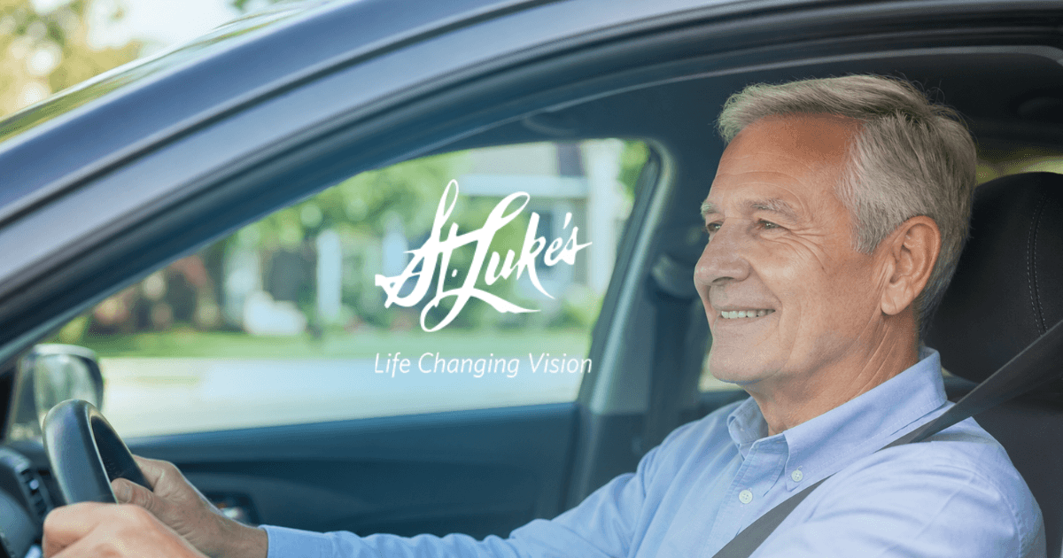Smiling mid-senior man driving confidently after cataract surgery, photographed from the side through the car window.